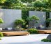 A tranquil outdoor workspace featuring modern noise reduction panels, blending seamlessly into a lush garden landscape with a hint of urban surroundings in the background.