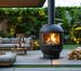 "An outdoor living area at dusk with an elegant eco-friendly stove, emitting a warm glow amidst lush greenery, symbolizing sustainable outdoor heating using renewable energy sources."