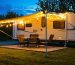 A scenic view of an RV campsite at dusk with an illuminated awning and solar-powered pathway lights creating a cozy and inviting outdoor space.
