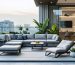 An urban balcony featuring modern collapsible outdoor furniture, including a folding table and modular bench with hidden storage, set against a city skyline backdrop.