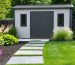 Stylish backyard storage shed with contemporary architecture, surrounded by vibrant landscaping including ornamental grasses and flowering shrubs, with an inviting stone pathway.