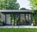 A contemporary backyard shed featuring large glass panels and angular rooflines, surrounded by lush landscaping with planters and climbing vines.