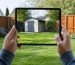 A homeowner using a tablet with augmented reality features to visualize a 3D shed overlay in their backyard, demonstrating the interactive potential of AR technology for designing storage solutions.