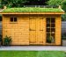 "Sustainable wooden shed with a living green roof, built from reclaimed wood in a garden setting."