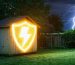 Artistic representation of a wooden shed in a backyard with a glowing protective shield, illustrating the concept of protection against power surges amidst a distant lightning storm.