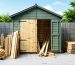 A partially constructed wooden shed utilizing green-tinted pressure-treated 2x4s stacked alongside untreated lumber, set against an outdoor backdrop emphasizing weather resistance.