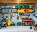 Organized shed interior with pegboard and slatwall holding tools, heavy-duty shelves with clear storage bins, overhead racks carrying a kayak and camping gear, and open floor space with a lawnmower and wheelbarrow, seen from the doorway in soft natural light.