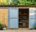 Partially built backyard shed with reclaimed wood walls, recycled corrugated metal roof, and bamboo shelves visible through the doorway, shot at eye level in golden-hour light with garden beds and trees in the background.