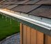 Close-up view of a shed roof with a metal J-channel drip edge guiding rainwater off the eave, with a gravel perimeter drain and lawn softly blurred in the background.