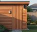 Modern cedar backyard shed with a mounted environmental sensor and compact security camera by the door, lit by golden hour light with a softly blurred garden and fence in the background.