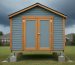 Reinforced backyard shed on elevated concrete piers with metal anchors and sealed doors under a stormy sky, with a suburban yard and windswept trees in the background.