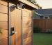 Smart lock and outdoor security camera mounted on a modern wooden garden shed door at golden hour, with a softly blurred backyard in the background.
