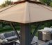 Close-up of a backyard gazebo soft-top canopy showing stitched seams and water droplets on the edge, photographed from a low angle at golden hour with patio furniture, grill, and garden blurred behind.