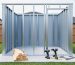 Partially built backyard shed with light gauge galvanized steel stud framing on a concrete pad, small stack of lumber and tools in the foreground, and softly blurred lawn, trees, and fence in the background under bright overcast light.