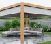 Modern backyard pergola with a waterproof retractable canopy shedding rain, keeping the lounge seating beneath dry, with wet patio and garden visible under an overcast sky.