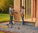 Partially assembled backyard shed on a level gravel foundation with tools arranged in the foreground and two people aligning a wall panel at golden hour; cleared perimeter and stacked panels softly blurred in the background.