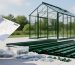 “Hands holding a rolled greenhouse instruction sheet next to hardware and a partially assembled green greenhouse frame in daylight”