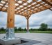 Close view of a backyard pergola’s posts anchored with heavy-duty brackets and concrete footings on a patio surface under an overcast sky.