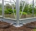 Close view of a greenhouse base frame secured with ground anchors and tension straps on a home property to prevent wind damage.