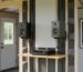 Inside a backyard shed man cave showing speakers and acoustic soundproofing panels around the walls with a compact audio receiver setup.