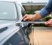 Homeowner measuring a vehicle’s dimensions with a retractable tape measure to plan a carport fitment.