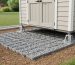 Backyard view of a 7x7 shed foundation kit with interlocking grid panels filled with gravel and adjustable support feet under a small shed.