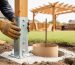 Close view of a wooden pergola post anchor and cardboard tube concrete footing form set in a deep dug hole in a yard.