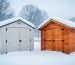 Resin and wood storage sheds side by side in a snow-covered yard during a winter storm, showing winter roof and wall conditions.