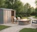 Metal storage shed next to a stone fire table with stacked firewood and a landscaped patio area in a backyard.